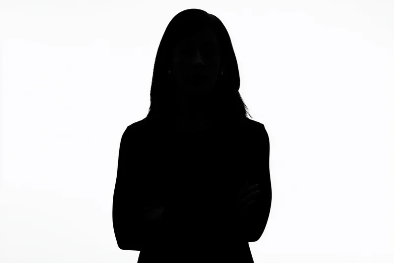 Silhouette of a woman standing with arms crossed against a white background