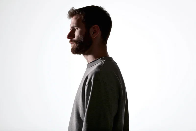 Bearded man in profile view wearing gray sweater against white background