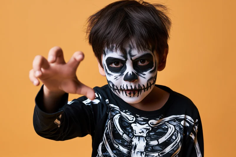 Young boy in skeleton costume making claw gesture against orange background