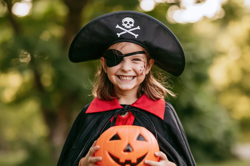 Young girl in pirate costume holding jack-o-lantern outdoors during halloween celebration