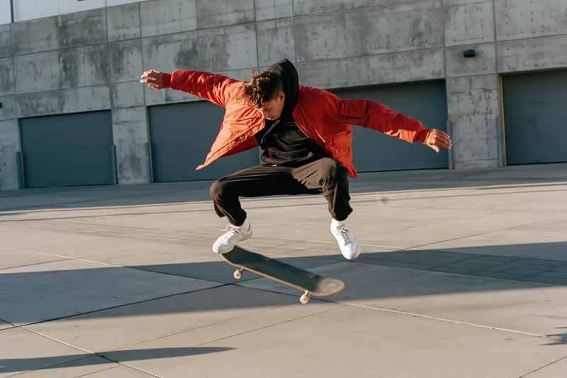 Young male skateboarder performing kickflip midair on concrete pavement in urban setting