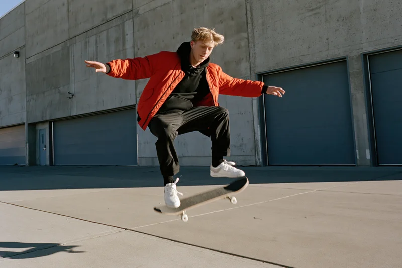 Young male skateboarder performing kickflip midair in urban setting