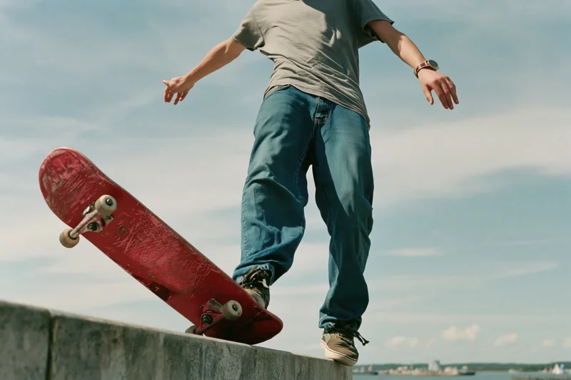 Young male skateboarder performing trick on concrete ledge outdoors