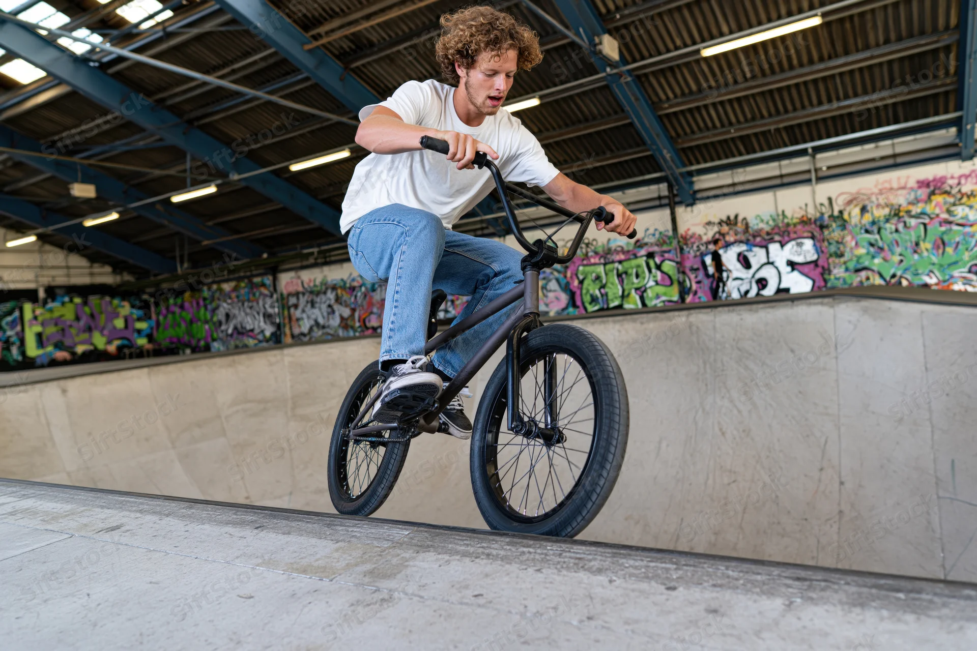 Young man riding bmx bike on concrete ramp in indoor skatepark