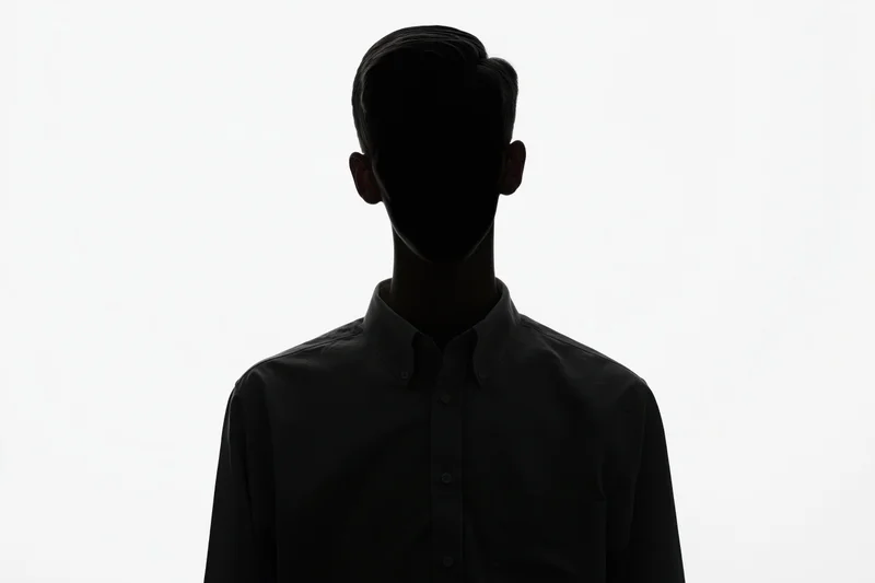 Silhouette of a young man standing still in shadow against white background wearing a dark button-up shirt