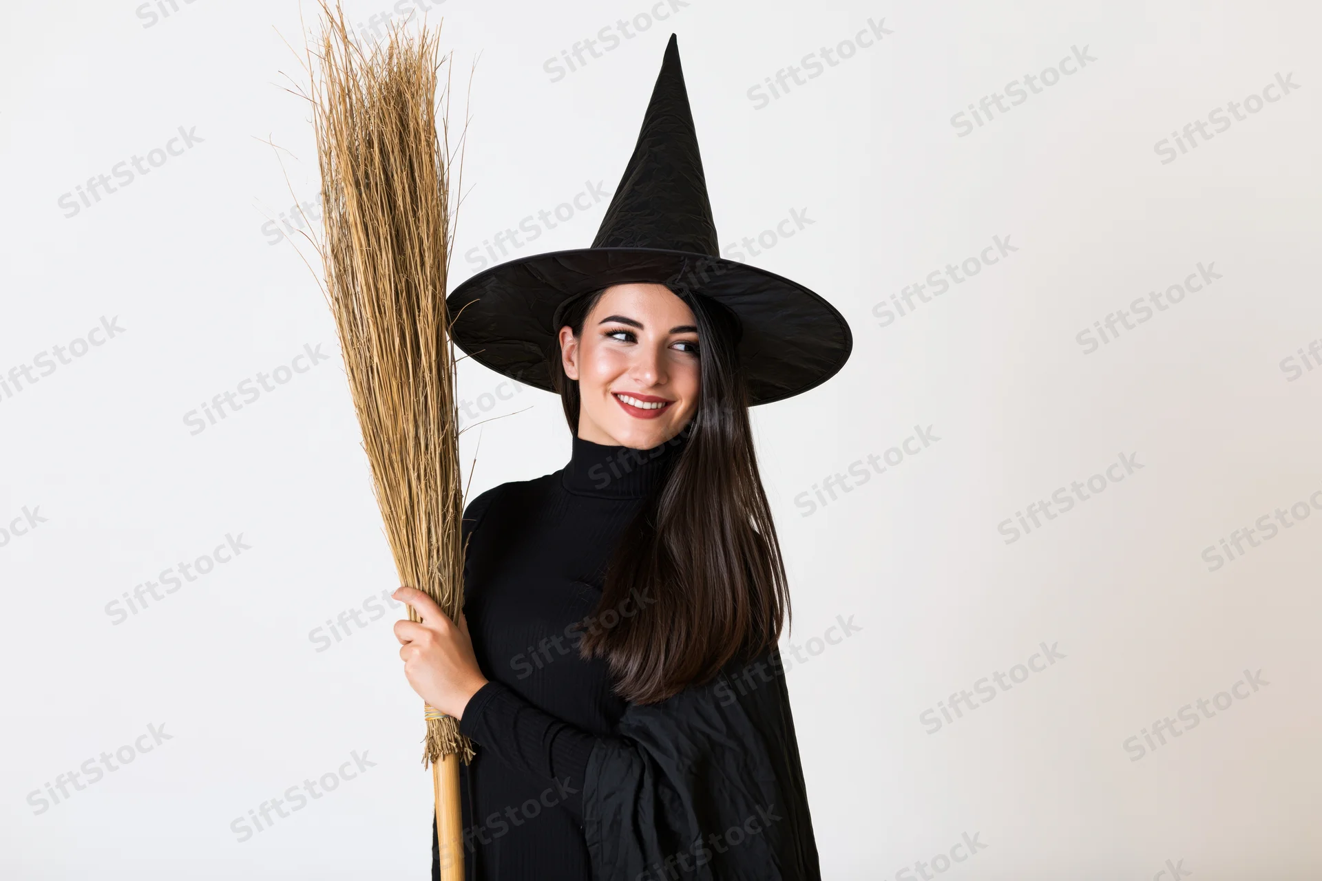 Young woman in witch costume holding straw broom against white background