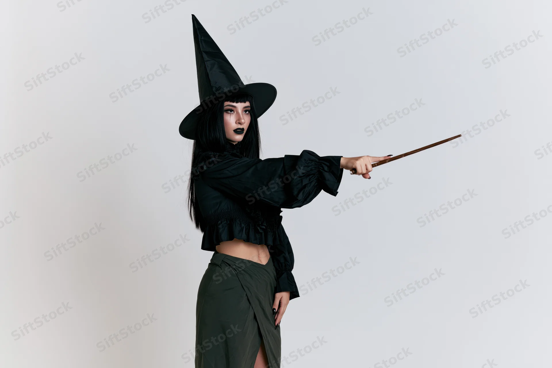 Woman in witch costume pointing wand in studio