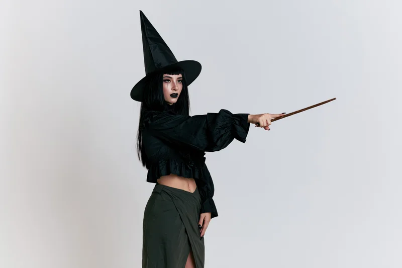 Woman in witch costume pointing wand in studio