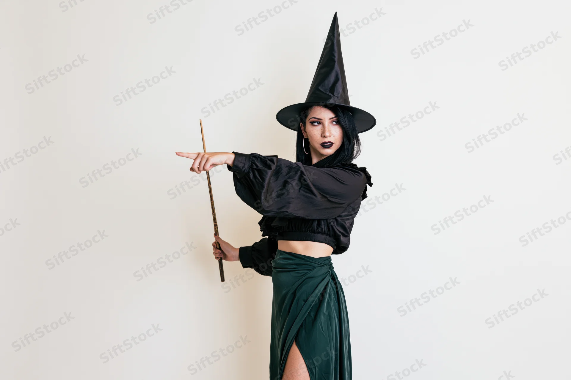 Woman in witch costume pointing with wand against white background