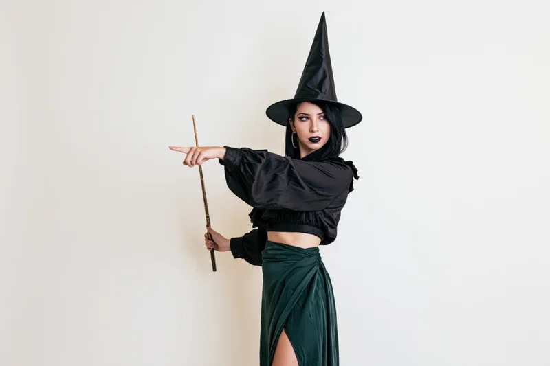 Woman in witch costume pointing with wand against white background