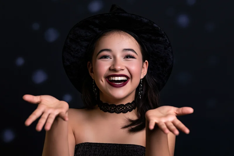 Young woman in witch costume smiling with open hands against dark bokeh background