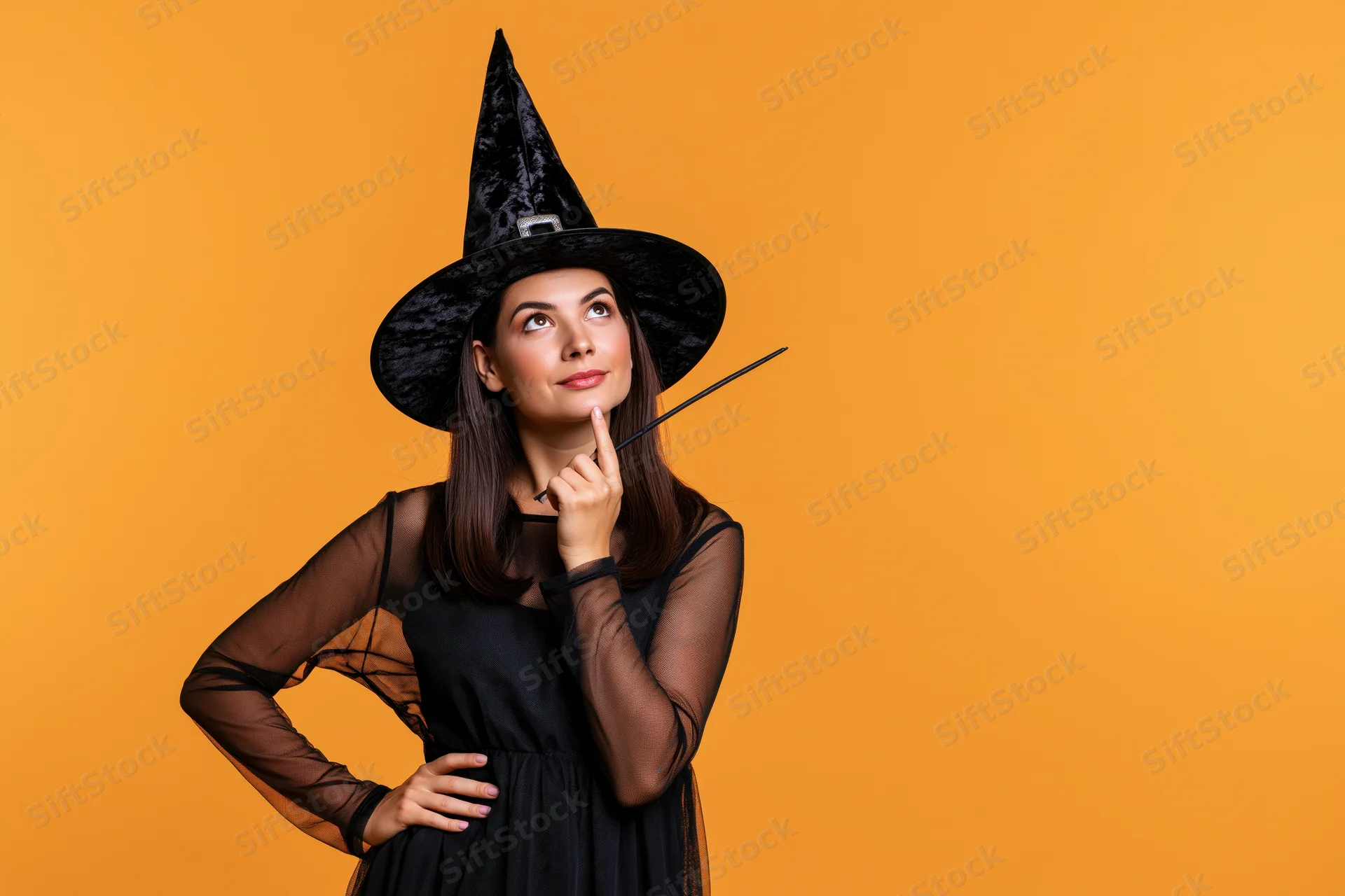Woman in black witch costume pointing finger to chin against orange background