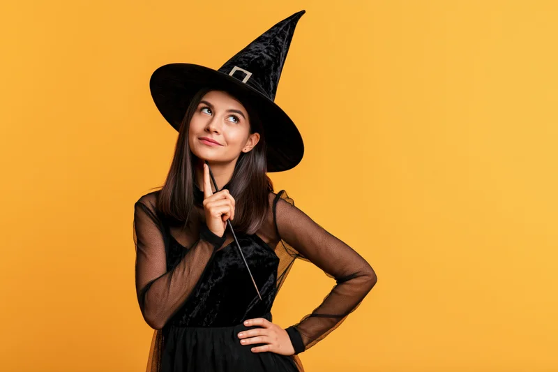 Woman in black witch costume holding wand and posing against orange background