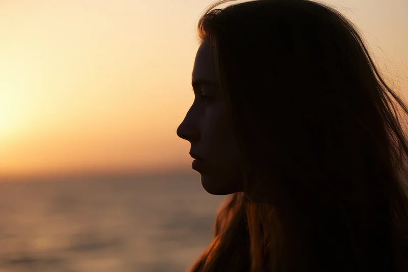 Young woman in side profile gazing forward at sunset over ocean