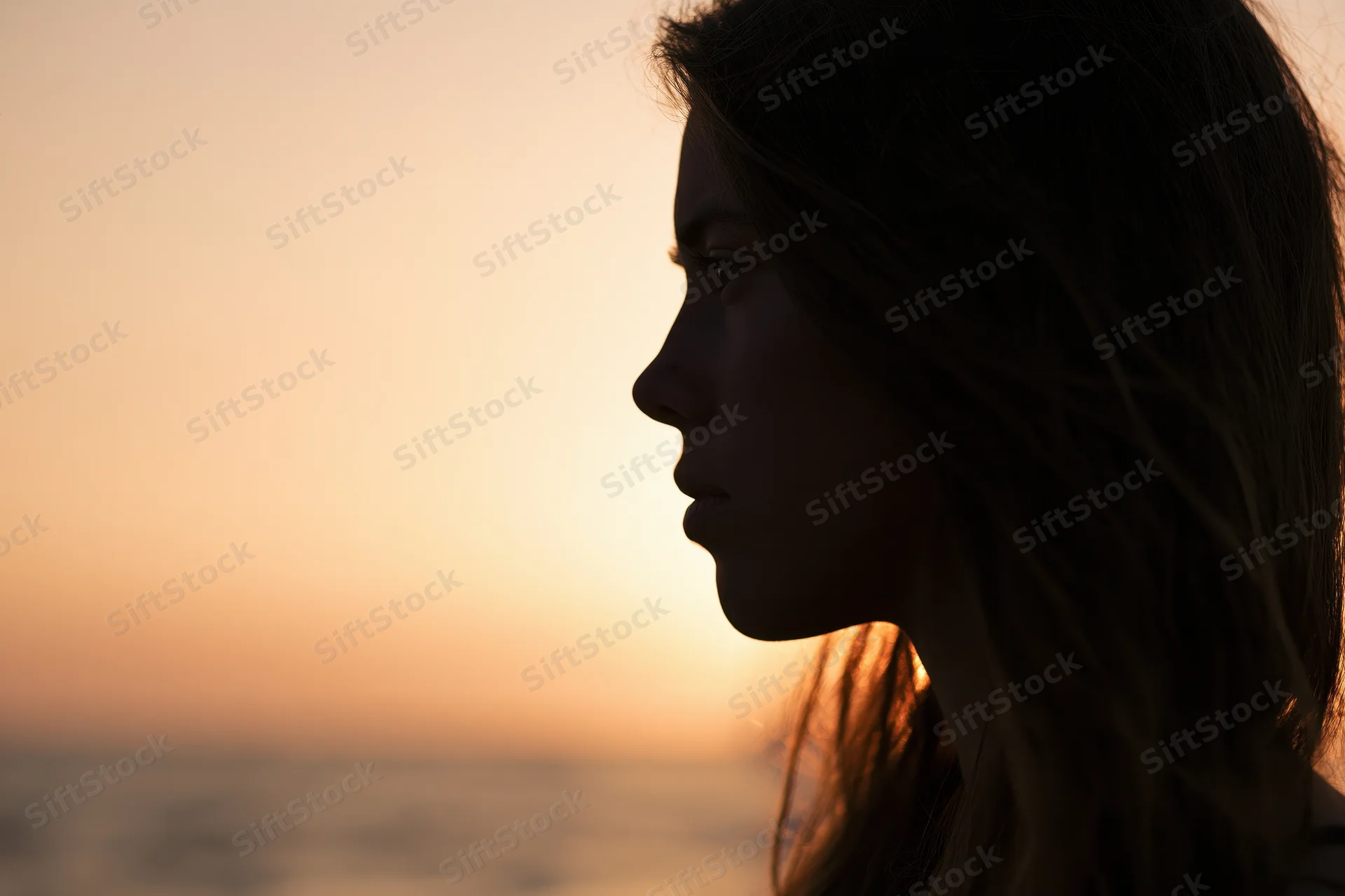 Young woman in side profile silhouetted against sunset over ocean
