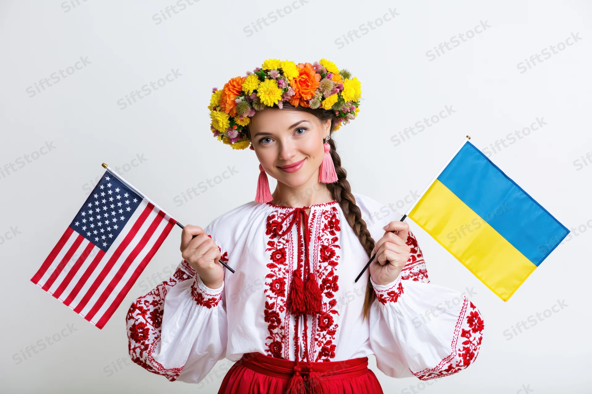 Young woman in traditional ukrainian vyshyvanka holding ukrainian and american flags in studio