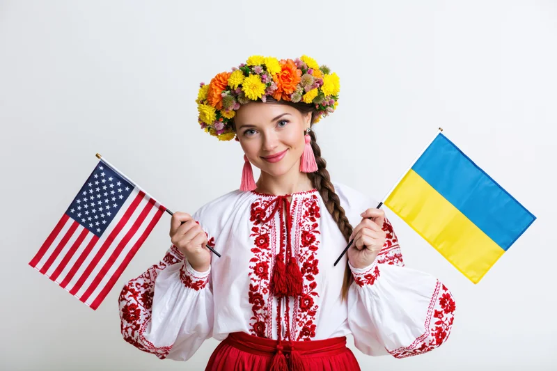 Young woman in traditional ukrainian vyshyvanka holding ukrainian and american flags in studio