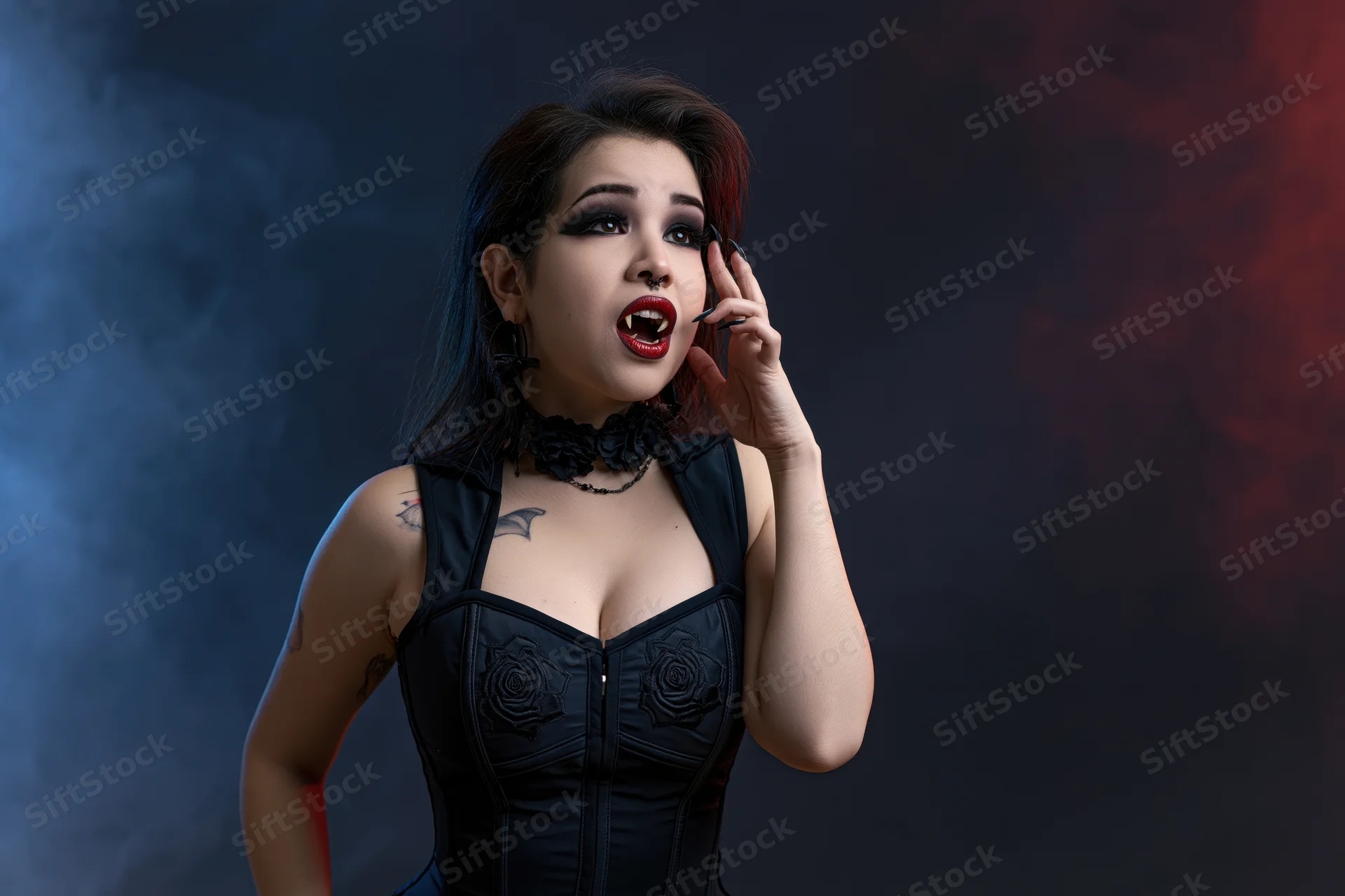 Woman in vampire costume posing dramatically with hand near face in smoky studio