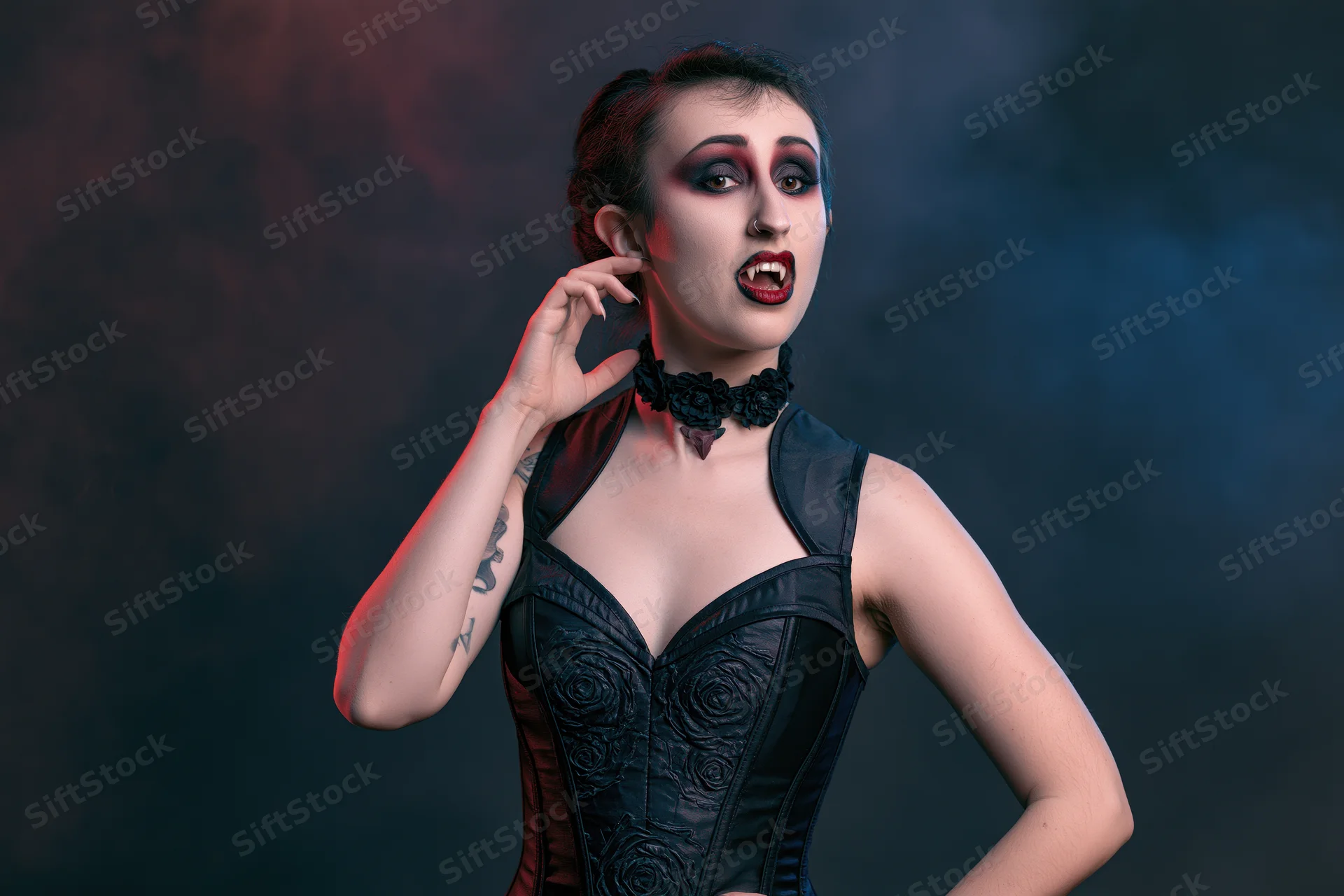 Woman in vampire costume posing dramatically with hand near neck in smoky studio