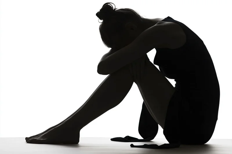 Silhouette of a woman sitting on the floor with knees pulled to chest and head resting on arms