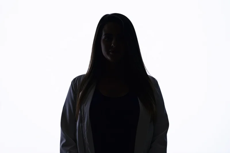 Silhouette of a young woman standing facing the camera with a subtle smile against a white background