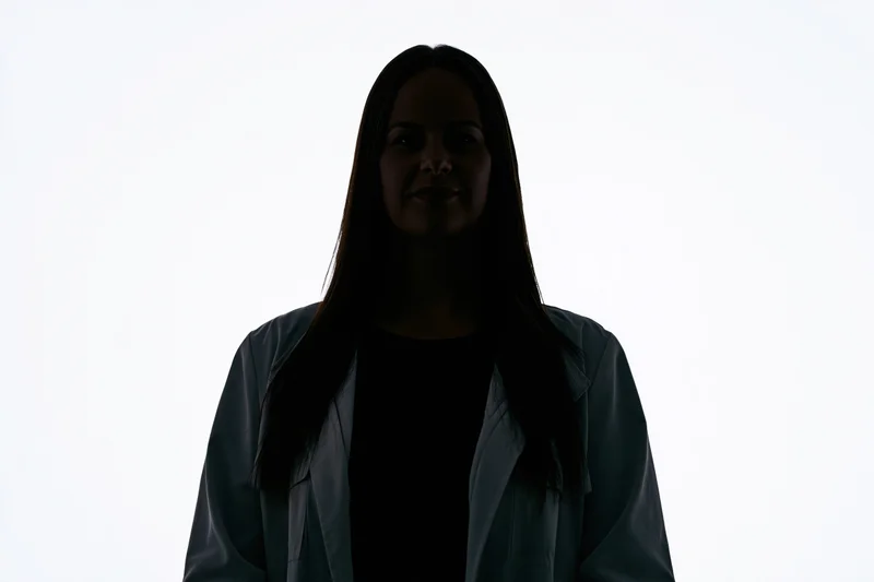 Silhouette of a woman standing facing camera with subtle smile against white background