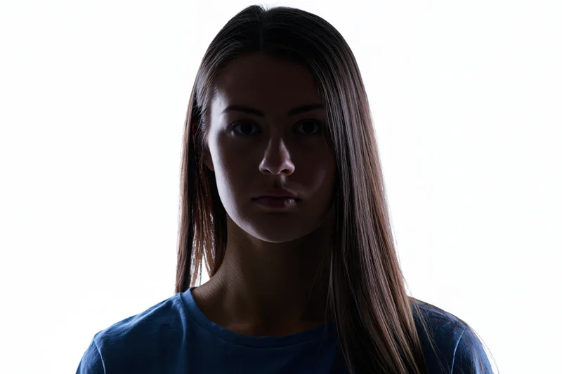 Young woman with long straight hair in silhouette against white background, facing camera with neutral expression
