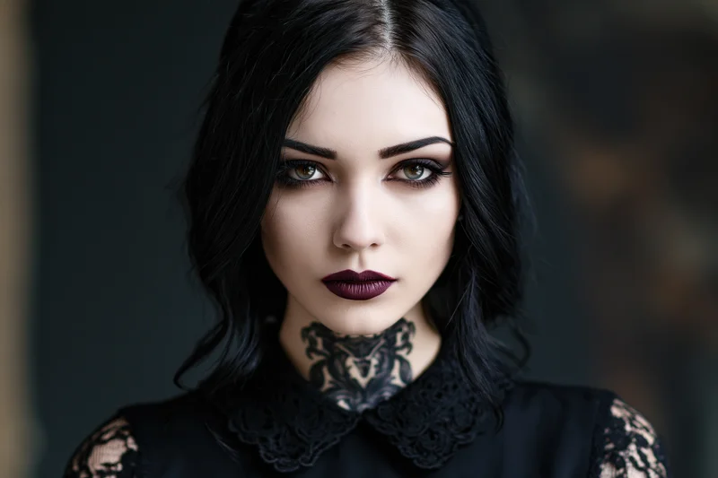 Young woman with dark gothic makeup and neck tattoo gazing directly at camera in black lace blouse
