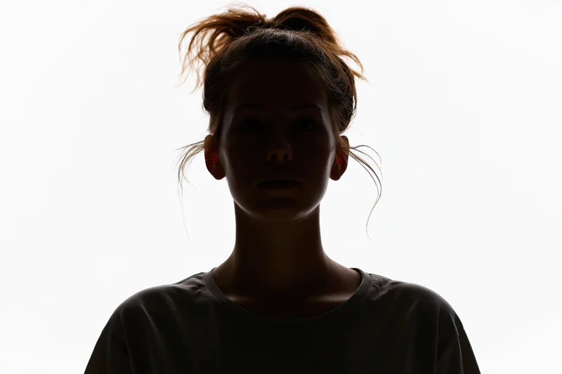 Silhouette of a young woman facing forward with hair in a bun against white background