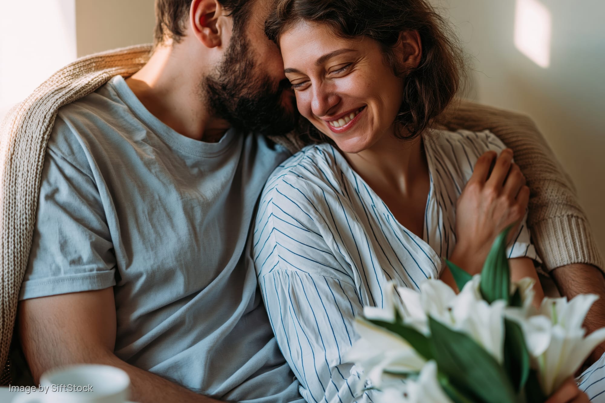 Couple embracing closely on a couch indoors with flowers and soft sunlight