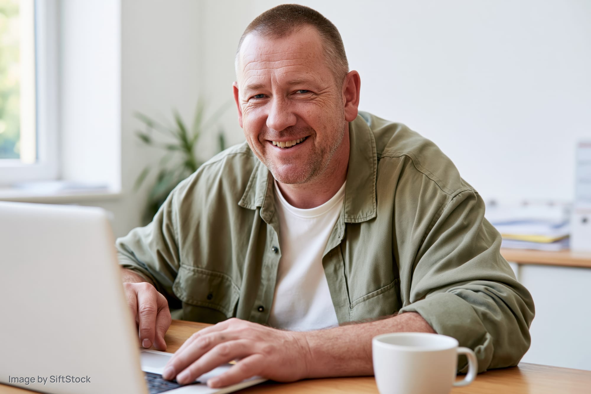 Man smiling while using laptop at wooden desk in home office
