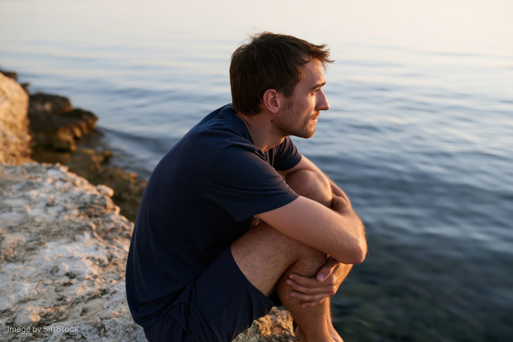 Man sitting on a rock ledge above the sea at sunset