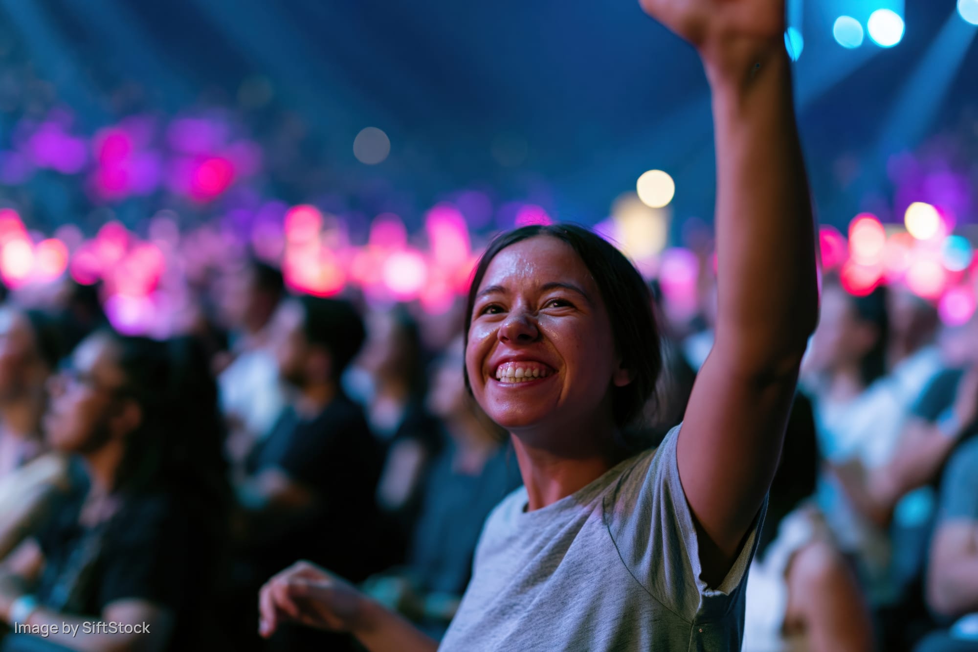 Woman smiling with raised fist in concert audience under stage lights