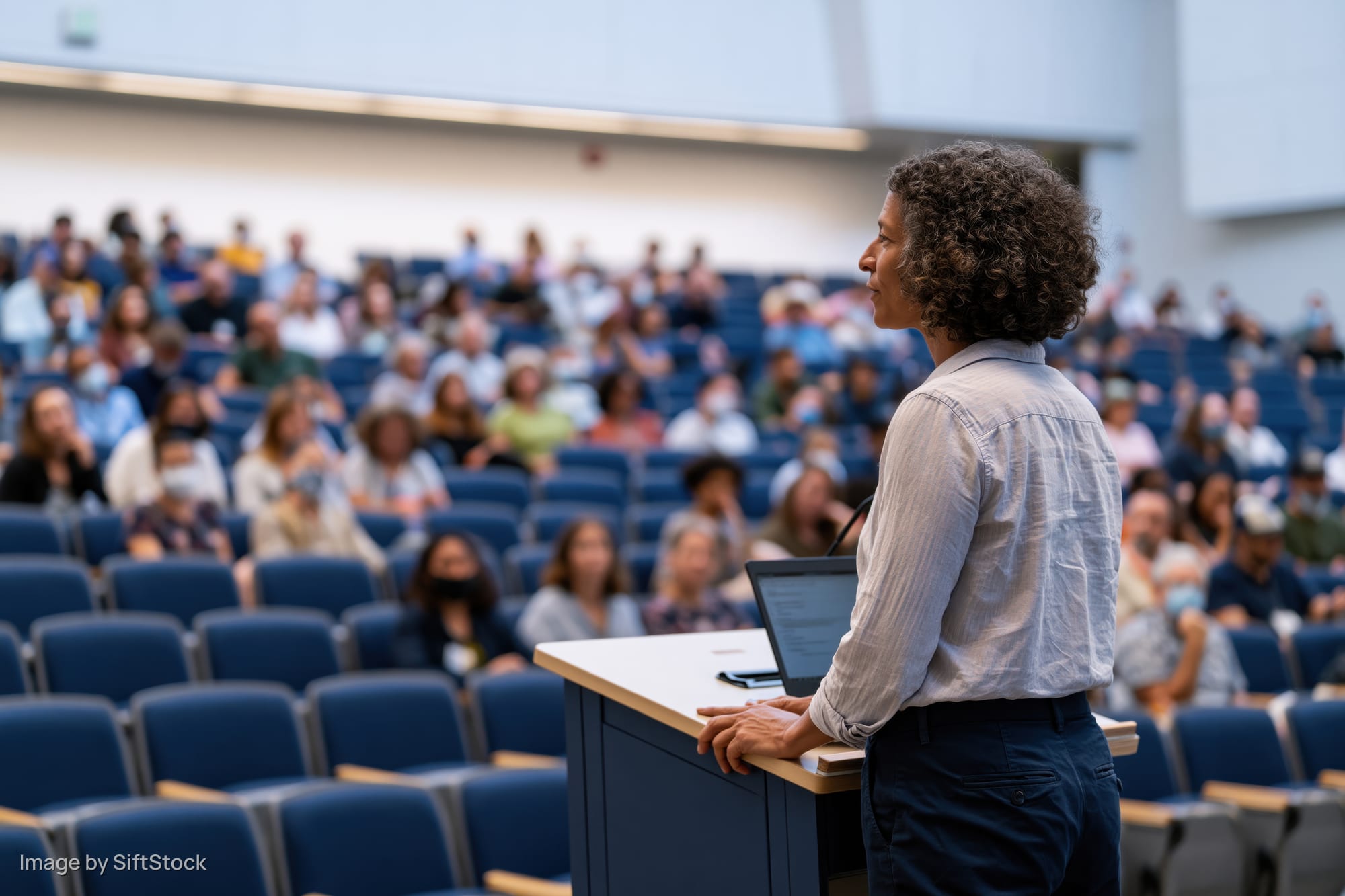 Woman speaker at podium addressing audience in lecture hall