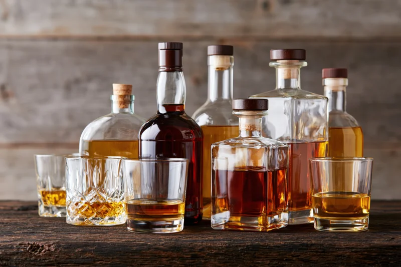 Whiskey and liquor bottles arranged with glasses on a wooden table