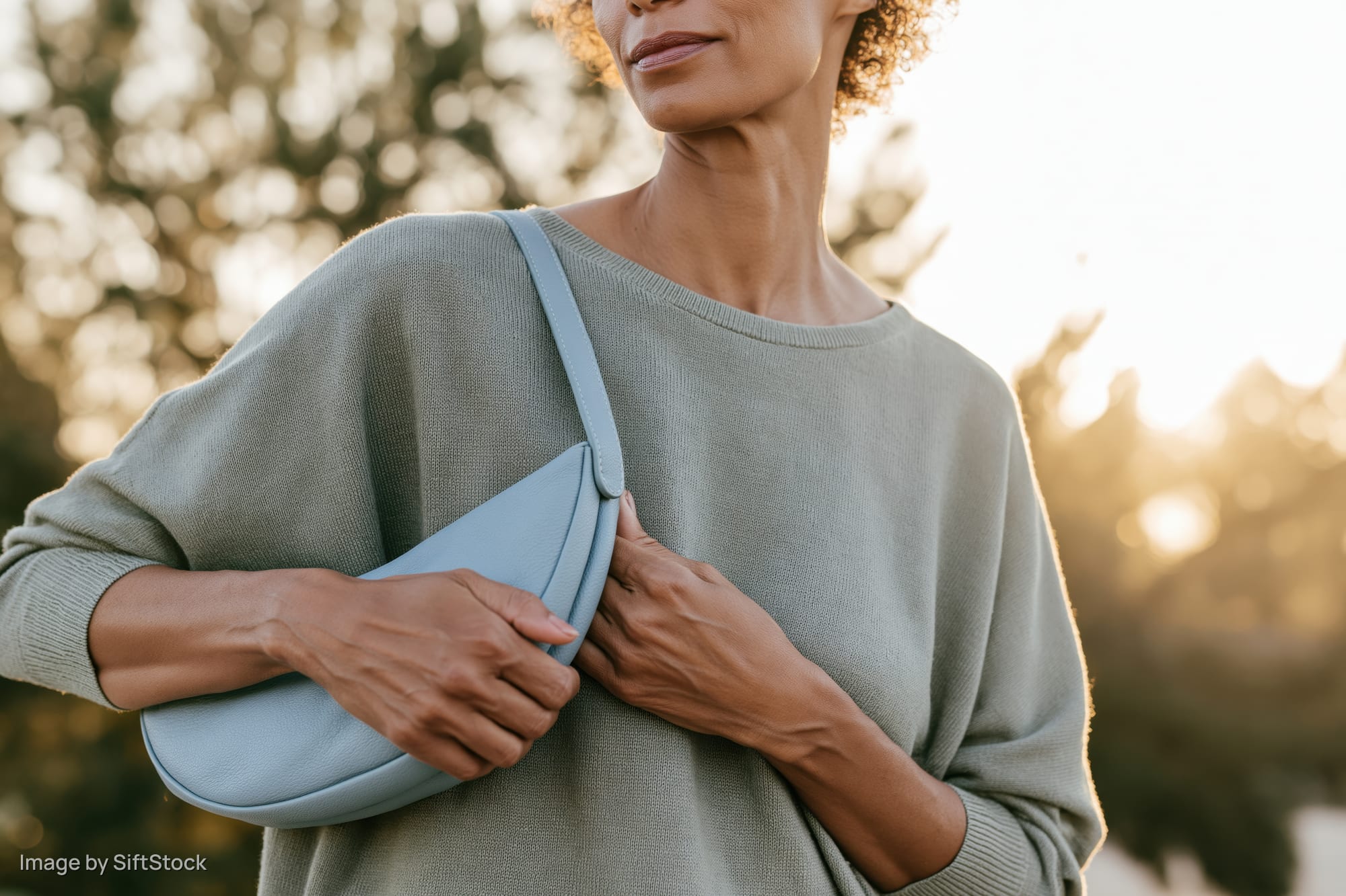 Woman holding light blue handbag over shoulder in outdoor setting at golden hour