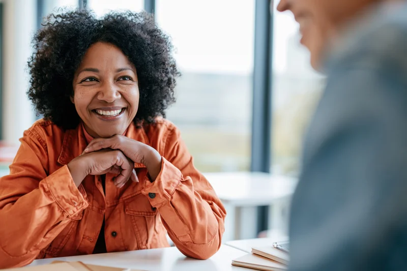 Woman smiling during conversation at cafe table with colleague