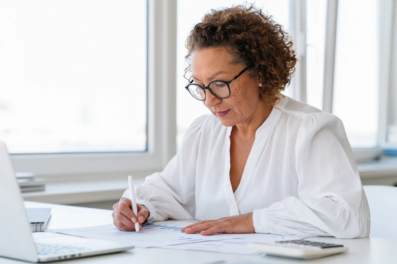 Woman writing on financial documents at office desk by window