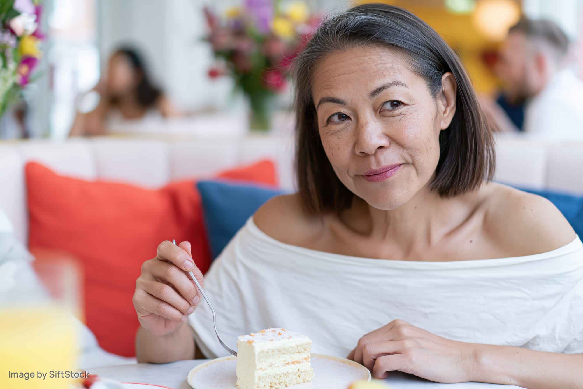 Woman eating cake in a cafe booth with colorful cushions and floral decor