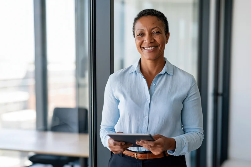Woman smiling while holding tablet in modern office near glass window