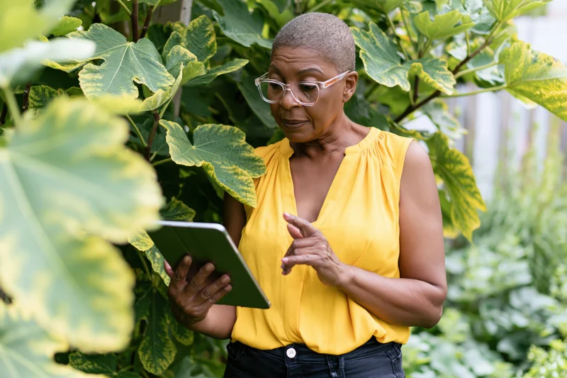 Woman using tablet in garden surrounded by green foliage