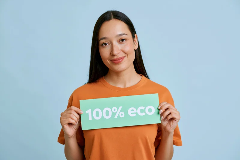 Woman holding green sign with 100% eco text in orange tshirt against light blue background