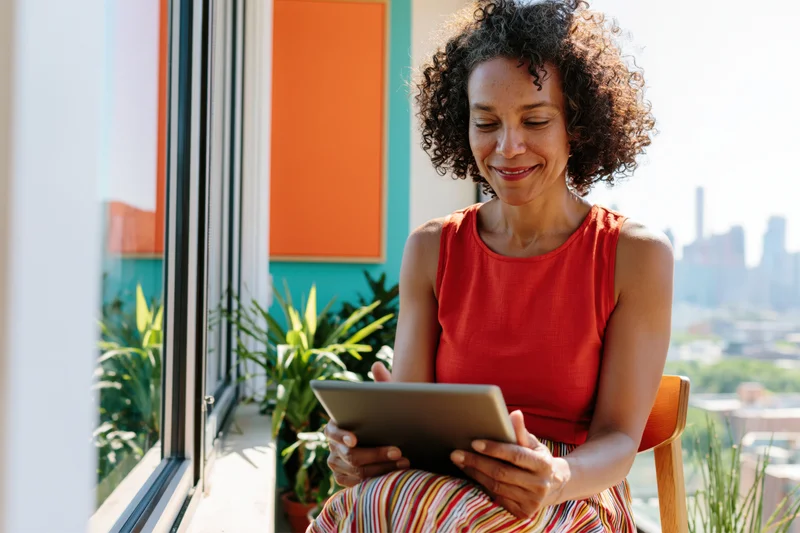 Woman smiling while using tablet on balcony overlooking cityscape
