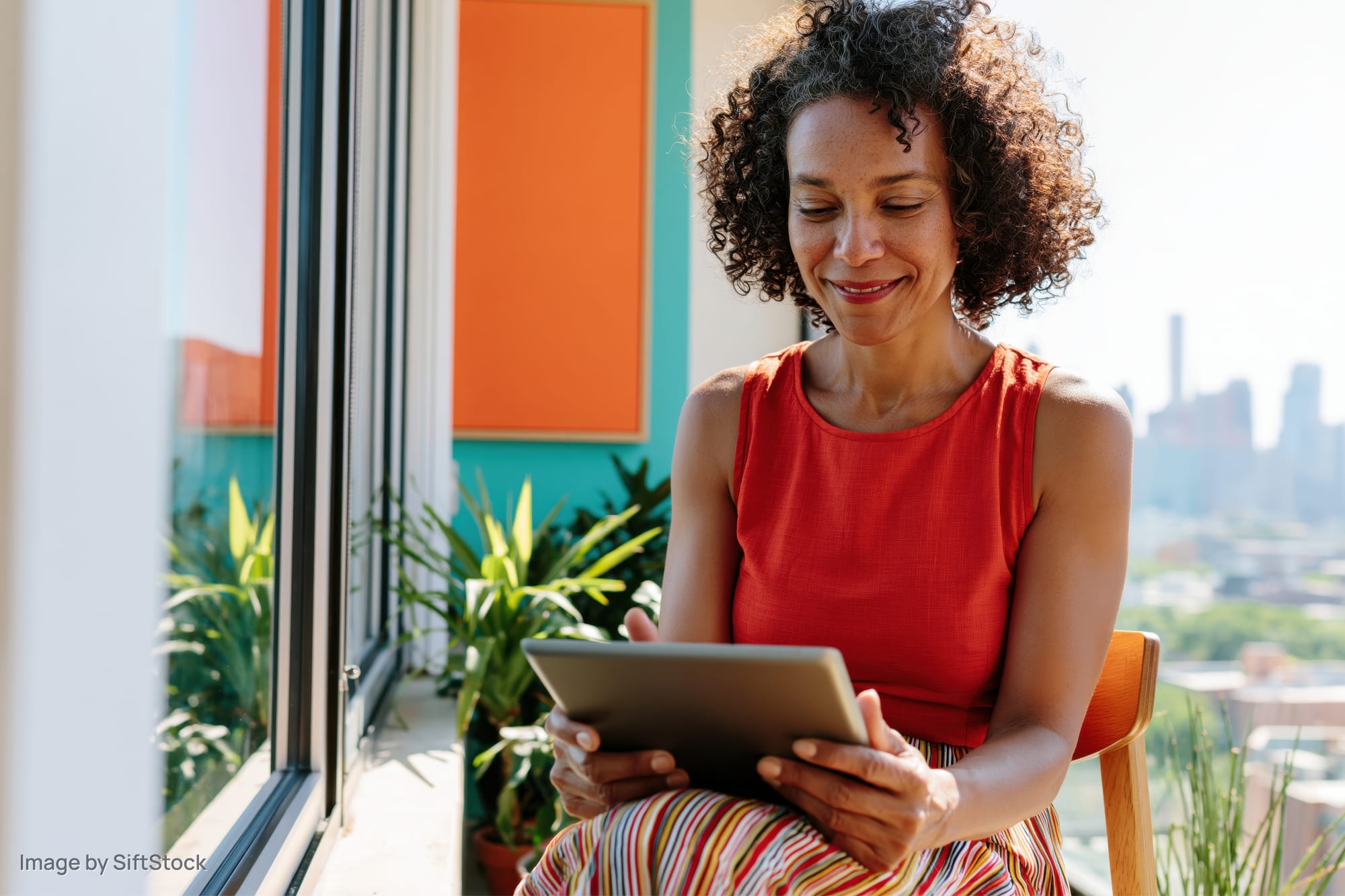 Woman smiling while using tablet on balcony overlooking cityscape