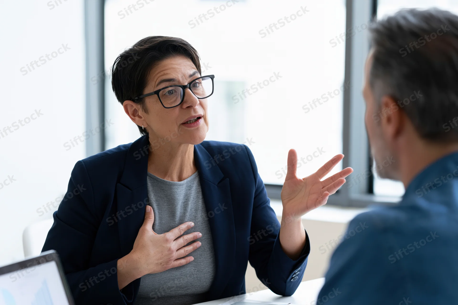 Woman in navy blazer gesturing during business meeting at office desk