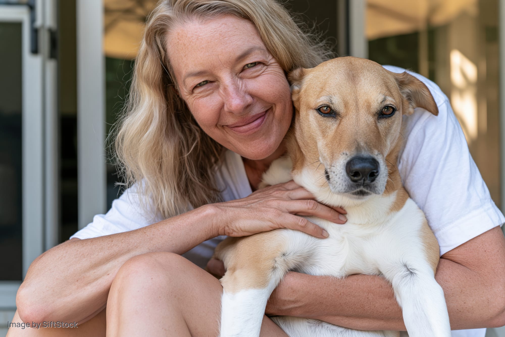 Woman hugging a tan and white dog on a porch while smiling