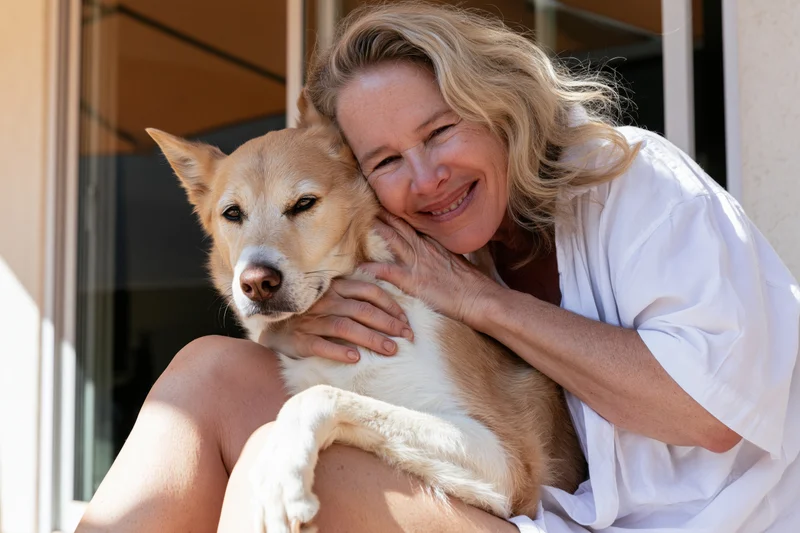 Woman hugging a tan dog on her lap outdoors on a sunny porch