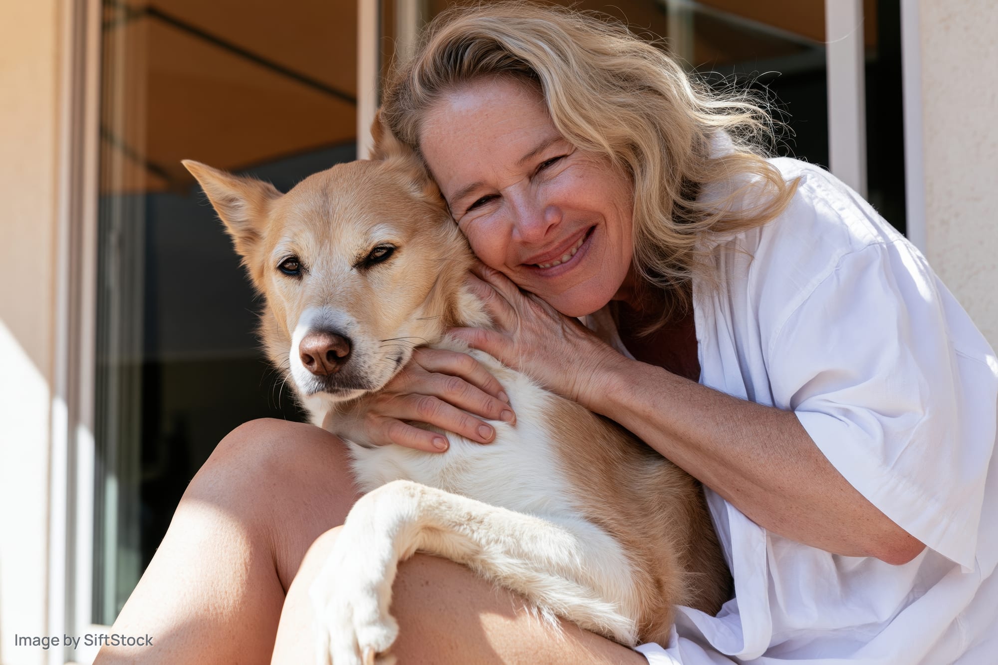 Woman hugging a tan dog on her lap outdoors on a sunny porch