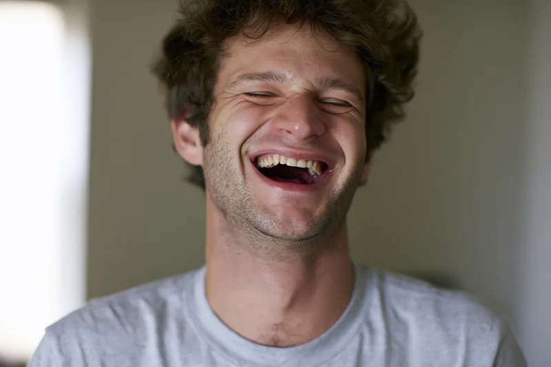 Young man laughing with mouth open and eyes squinting indoors