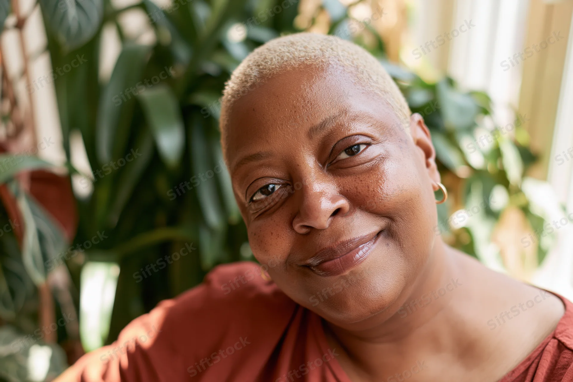 Close-up portrait of a smiling black woman with short blond hair indoors near green plants